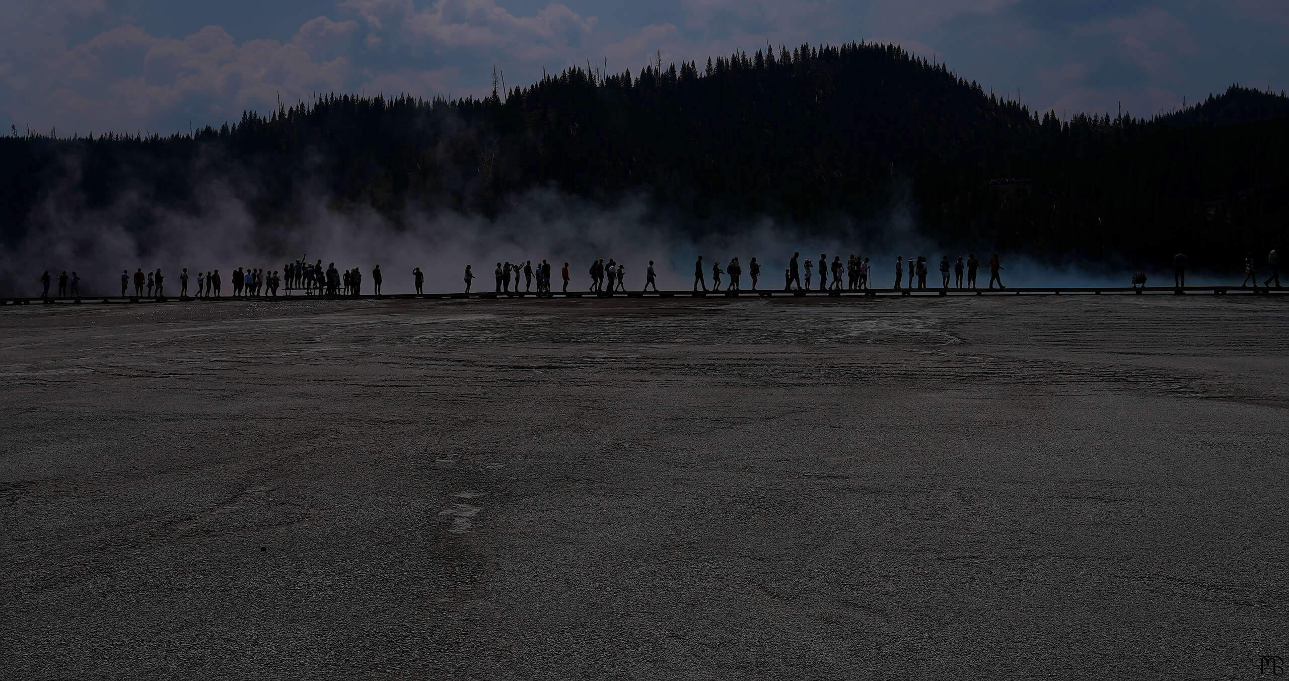 A silhouetted view of people walking near the Grand Prismatic Spring