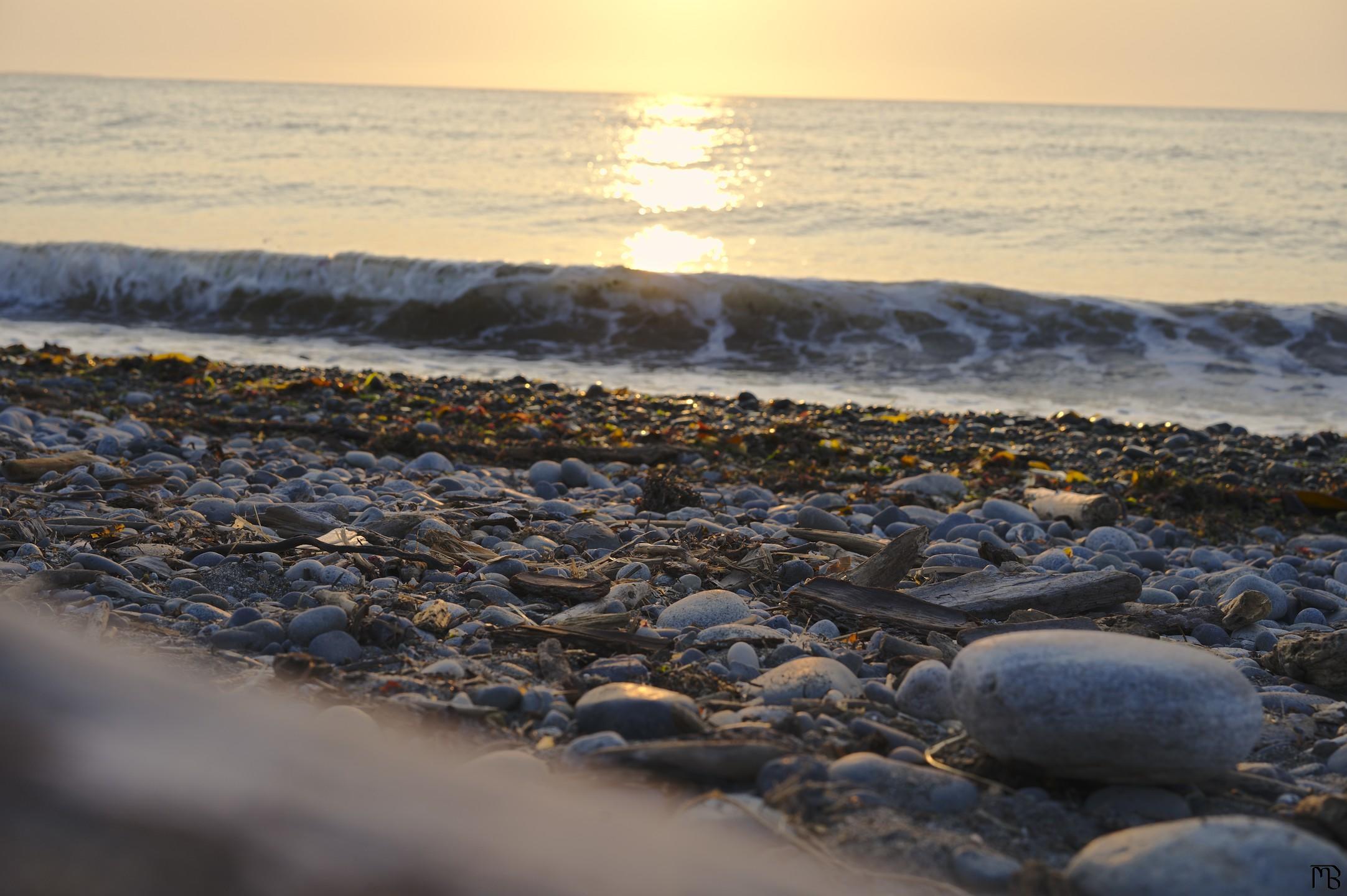 Sun reflecting on water near stony beach