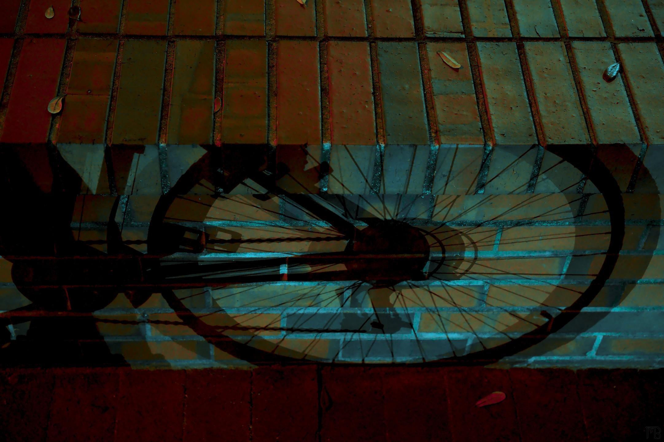 Arty red and blue shadow of bike wheel on brick