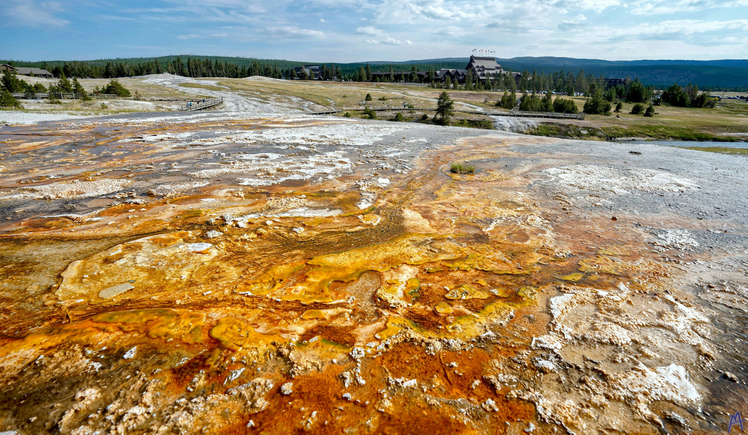 Orange and black hot spring runoff with a view of the lodge at Yellowstone