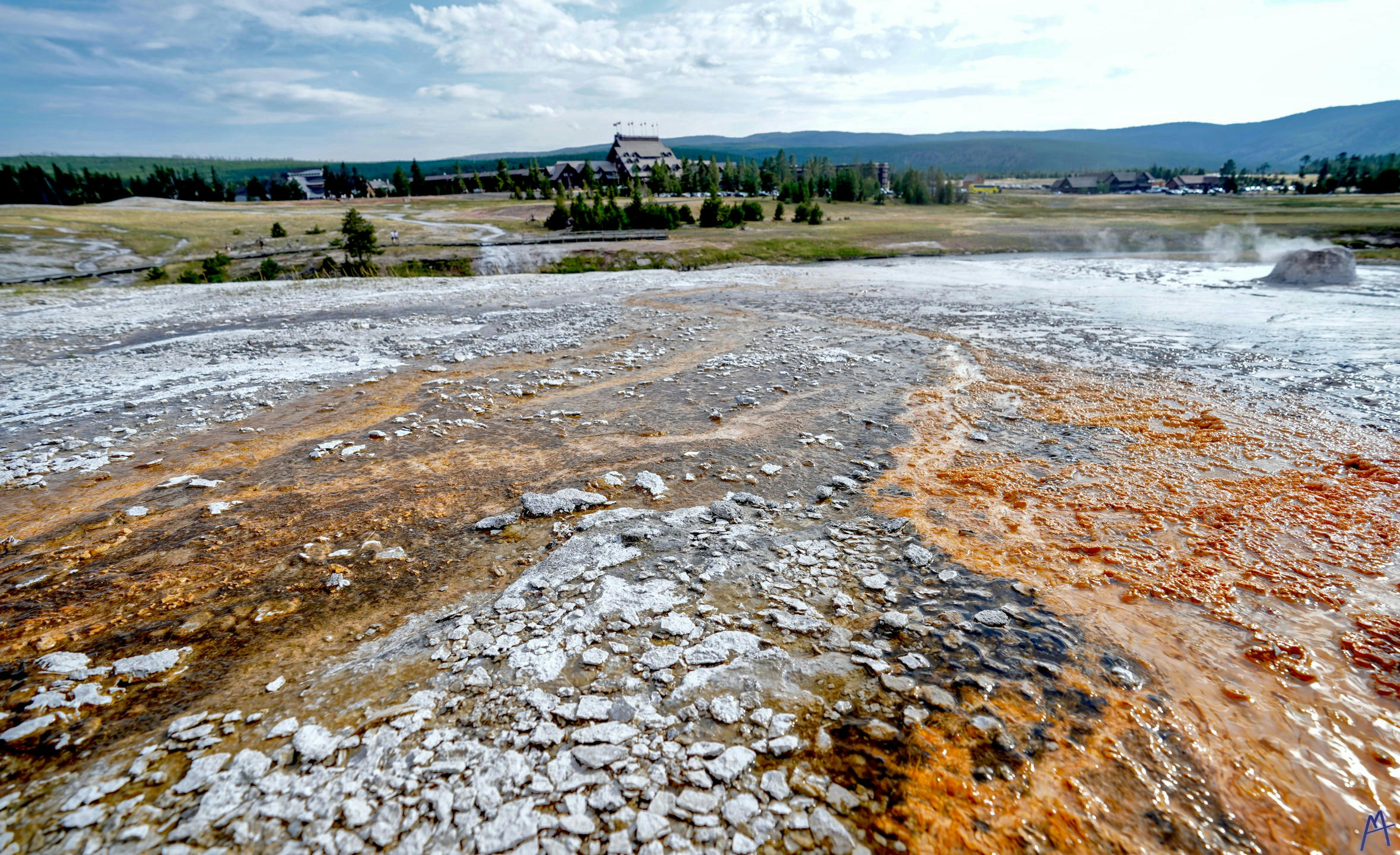 Swirls of orange and black hot spring runoff with a view of the lodge at Yellowstone