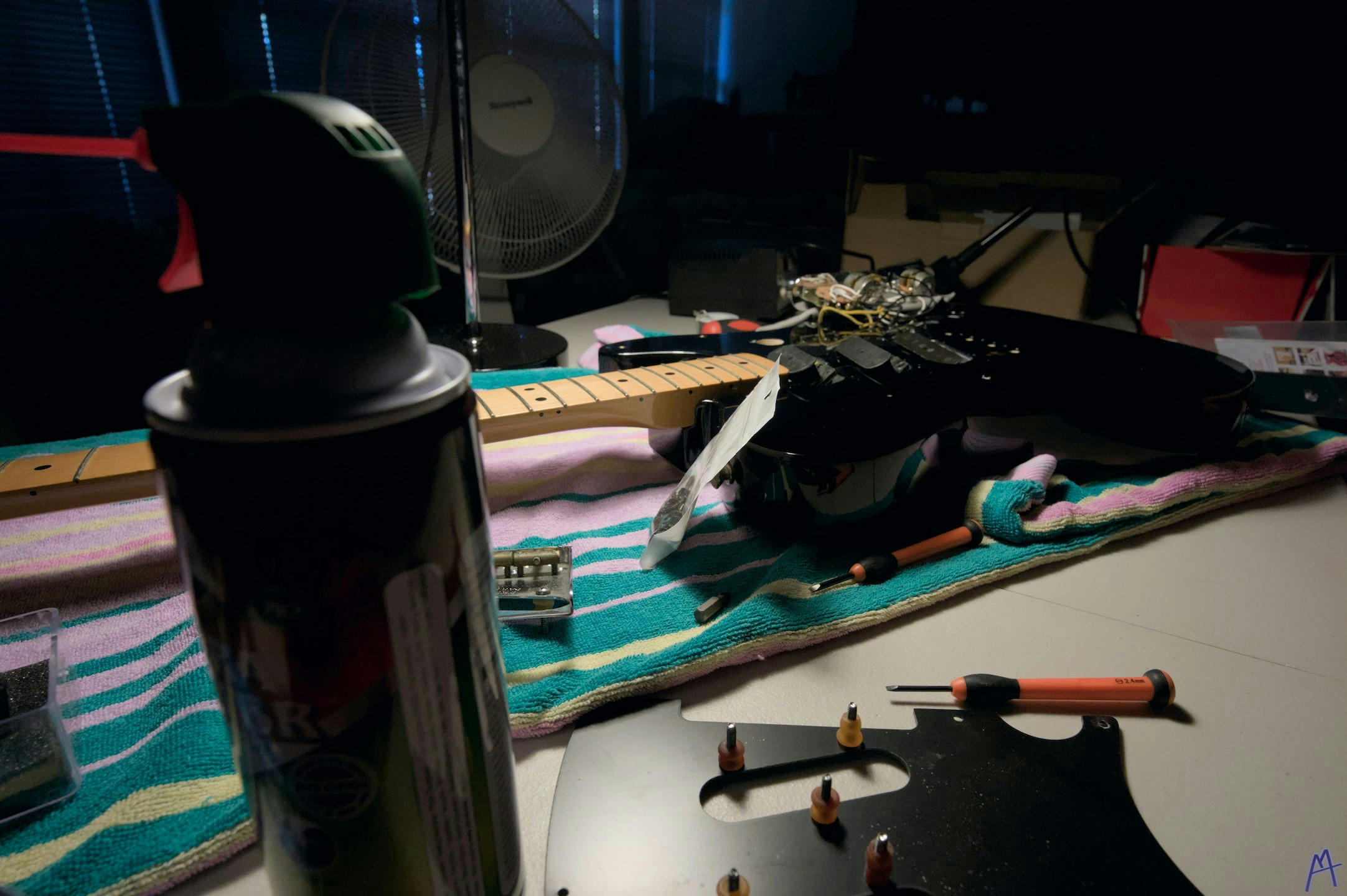 Black guitar on a workbench next to a can of air