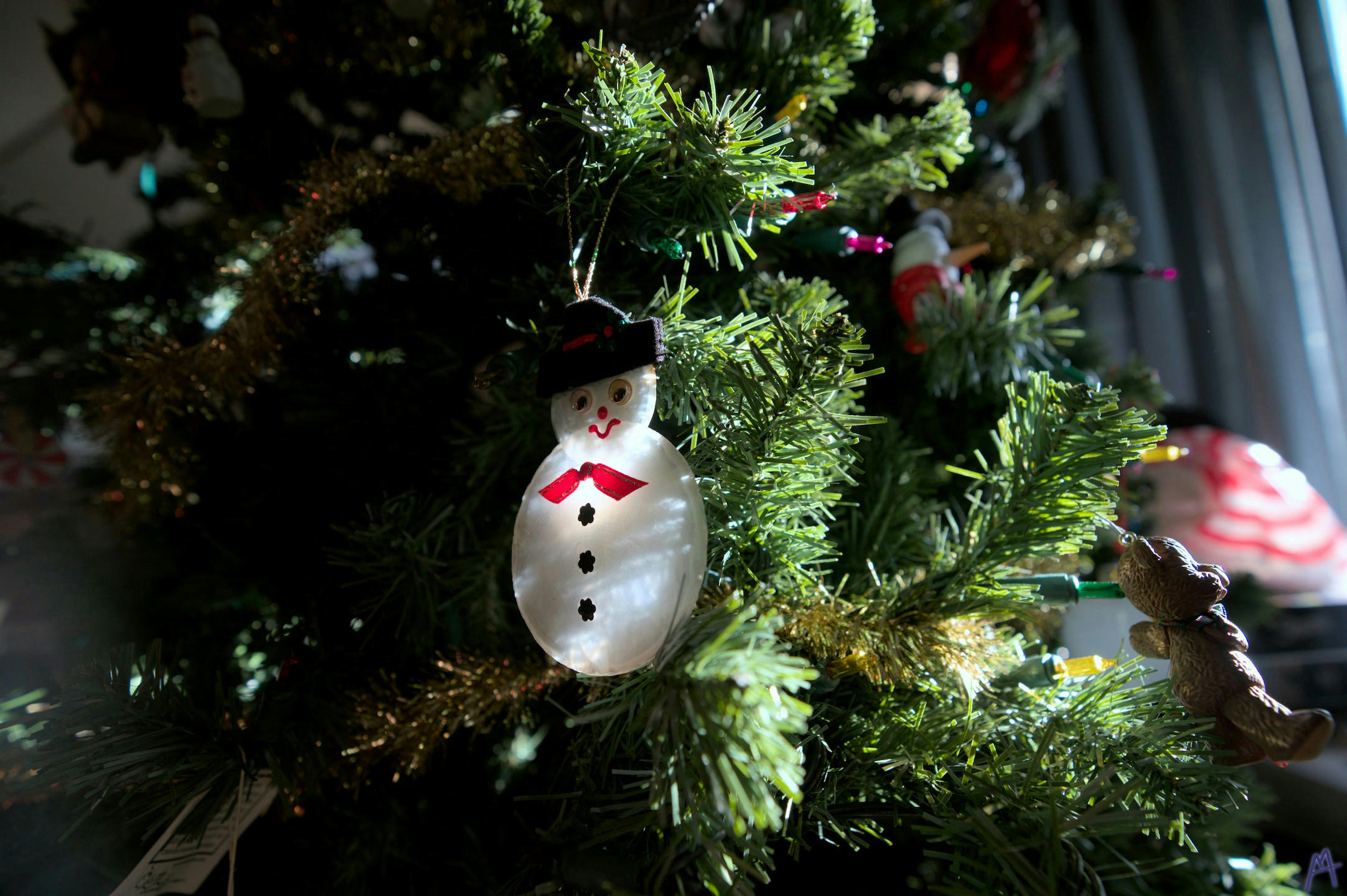 A white snowman ornament on a green Christmas tree and golden garland