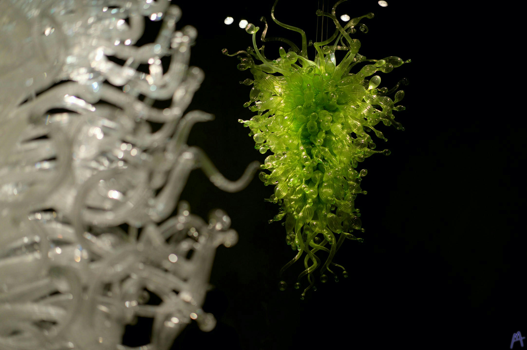 Green glass sculpture hanging behind a white sculpture